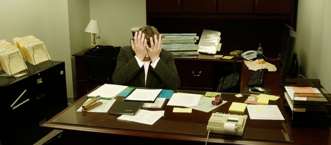 Frustrated man at a desk (Image by LaurMG [CC BY SA 3.0], via Wikimedia Commons)