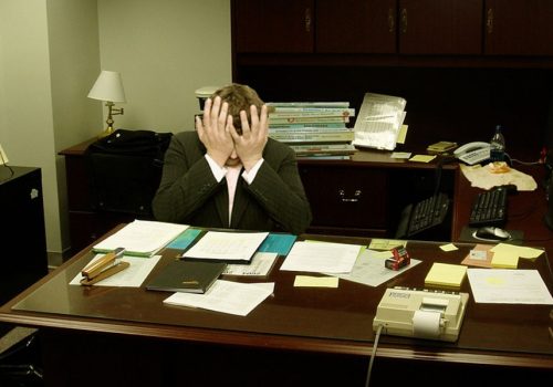 Frustrated man at a desk (Image by LaurMG [CC BY SA 3.0], via Wikimedia Commons)