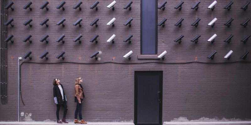 Women look at security cameras (adapted) (Image by Matthew Henry [CC0 Public Domain] via Unsplash)