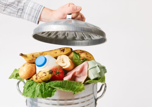 Hand Putting Lid On Garbage Can Full Of Waste Food