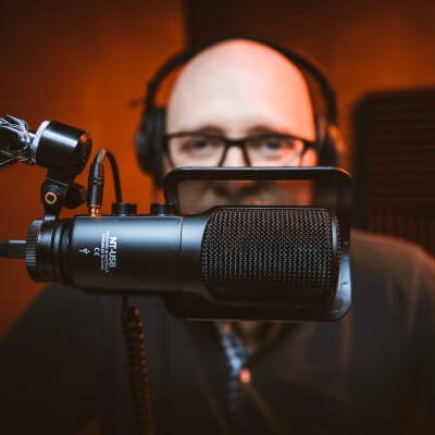 Titelbild zu Podcast-Hosting mit Podigee. Zu sehen ist ein Mann vor einem Mikrofon
