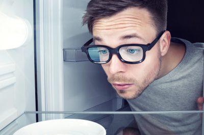 Student guckt in einen leeren Kühlschrank - Er braucht Rezepte für Studenten