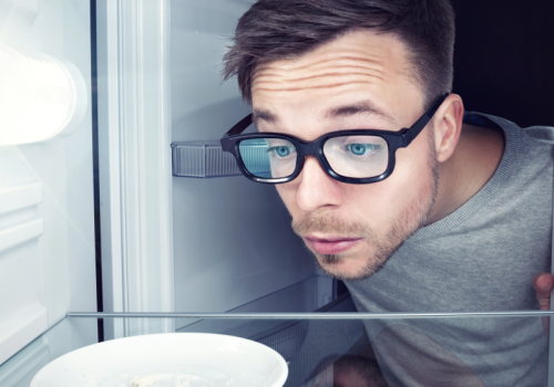 Student guckt in einen leeren Kühlschrank - Er braucht Rezepte für Studenten