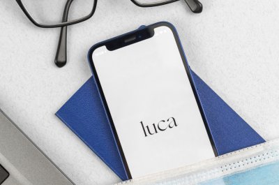 Smartphone hat die luca App geöffnet, über dem Smartphone liegt eine Brille, darunter eine Atemschutzmaske