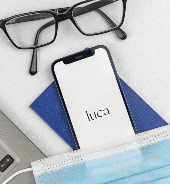 Smartphone hat die luca App geöffnet, über dem Smartphone liegt eine Brille, darunter eine Atemschutzmaske
