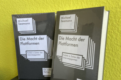 Zwei exemplare des Buches "Die Macht der Plattformen" vor gelben Hintergrund.