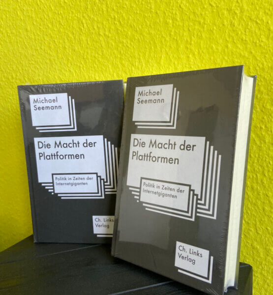Zwei exemplare des Buches "Die Macht der Plattformen" vor gelben Hintergrund.