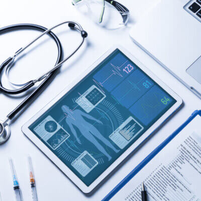 Beitragsbild Elektronische Patientenakte: Stethoskop, Tablet, Laptop und Fragebogen auf einem weißen Tisch.