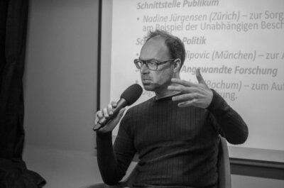 Christoph bieber auf einem podium, er spricht in ein Mikrofon und gestikuliert dabei