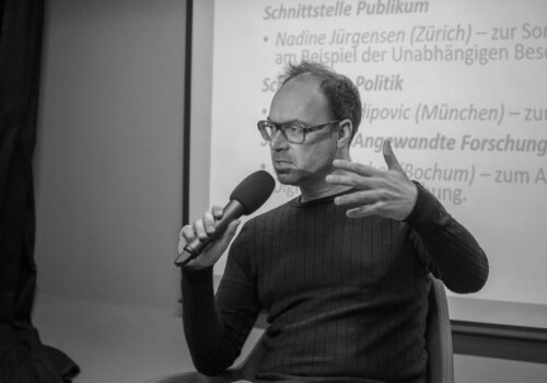 Christoph bieber auf einem podium, er spricht in ein Mikrofon und gestikuliert dabei