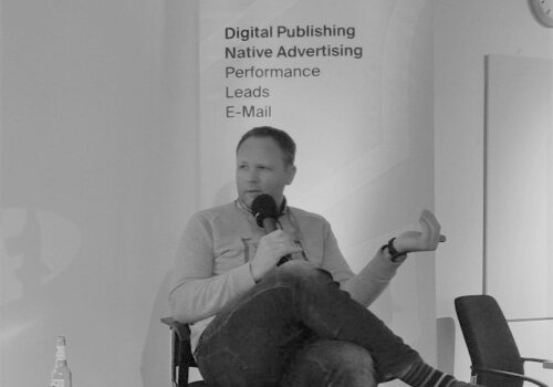 Clas Beese auf der Bühne der FinTech Week mit Mikro in der Hand. im Hintergrund ein Banner der Netzpiloten, er sitzt auf einem Stuhl mit Mikro in der Hand