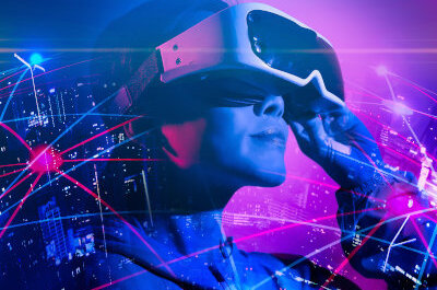 Eine Frau trägt eine Virtual Reality Brille. Um sie herum zeichnet sich eine vvernetzte Welt ab.