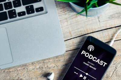 Beitragsbild Podcasts: Mobiltelefon auf einem hölzernen Schreibtisch mit Podcast-App im scr