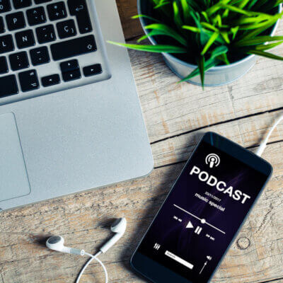 Beitragsbild Podcasts: Mobiltelefon auf einem hölzernen Schreibtisch mit Podcast-App im scr