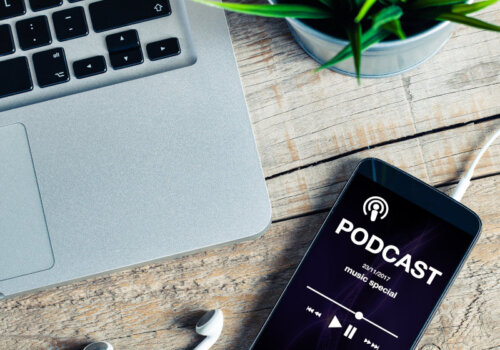 Beitragsbild Podcasts: Mobiltelefon auf einem hölzernen Schreibtisch mit Podcast-App im scr