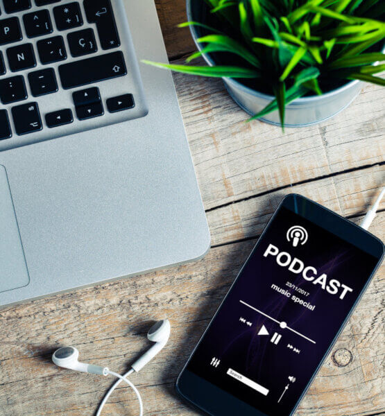 Beitragsbild Podcasts: Mobiltelefon auf einem hölzernen Schreibtisch mit Podcast-App im scr