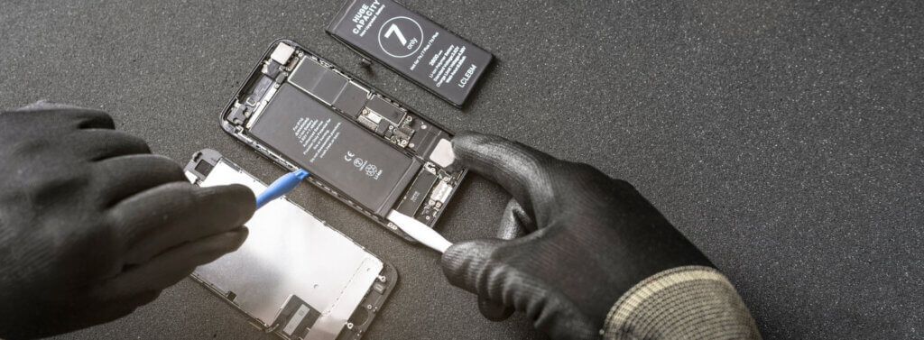 Ein auseinander gebautes Smartphone das von Händen in Handschuhen mit passendem Werkzeug repariert wird.