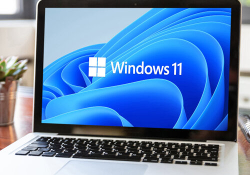 Laptop auf einem Tisch. Auf dem Bildschirm ist das Windows 11-Logo zu erkennen.