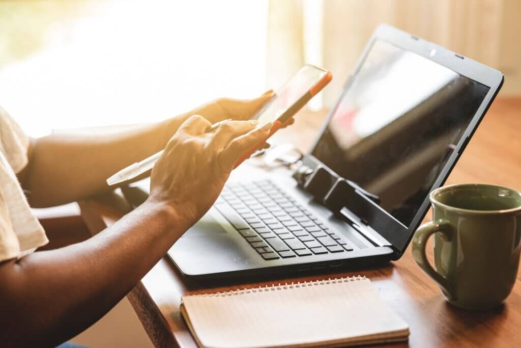 Person sitzt am Laptop, bedient zugleich aber auch das Smartphone.