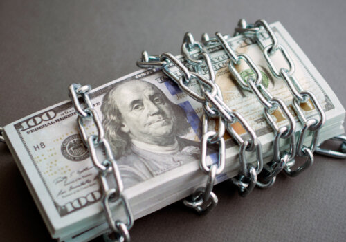 Geldbündel Dollar von Kette umwickelt, abstrakte Darstellung von eingefrorenen Konten und Geldströmen