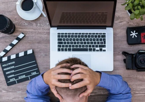 Mann fässt sich verzweifelt an den Hinterkopf mit dem Blick auf Laptop und andere Geräte.