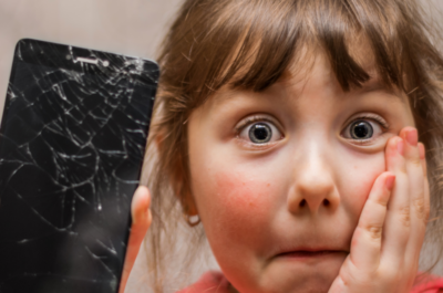 Ein erschrocken-trauriges Mädchen mit einem kaputten Smartphone in der Hand.