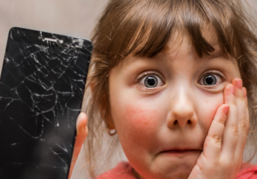 Ein erschrocken-trauriges Mädchen mit einem kaputten Smartphone in der Hand.
