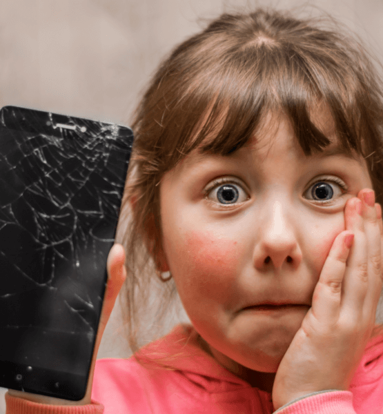 Ein erschrocken-trauriges Mädchen mit einem kaputten Smartphone in der Hand.