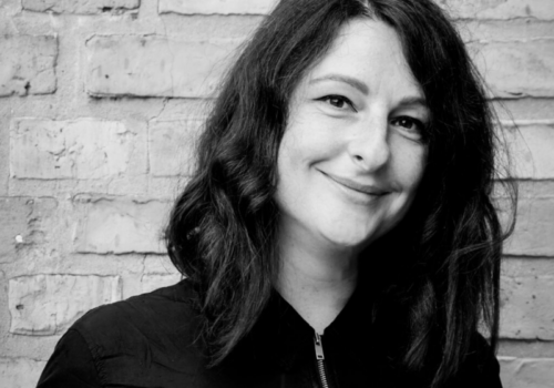 Anna Gleser im Portrait, sie trägt schwarz und lächelt schräg in die kamera