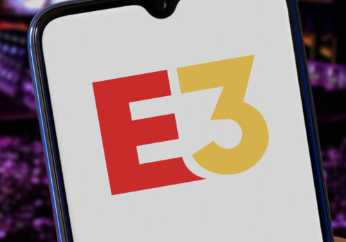 E3-Logo auf einem Smartphone. Im Hintergrund Publikum einer Veranstaltung.
