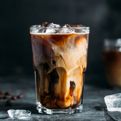 Ein Iced Coffee mit Milch. Die Eiswürfel sind nicht nur im Getränk, sondern auch auf dem Tisch.