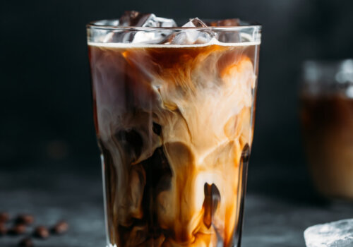 Ein Iced Coffee mit Milch. Die Eiswürfel sind nicht nur im Getränk, sondern auch auf dem Tisch.