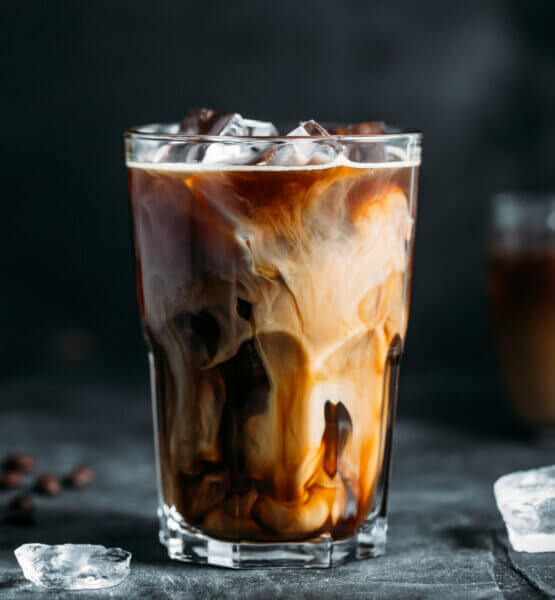Ein Iced Coffee mit Milch. Die Eiswürfel sind nicht nur im Getränk, sondern auch auf dem Tisch.