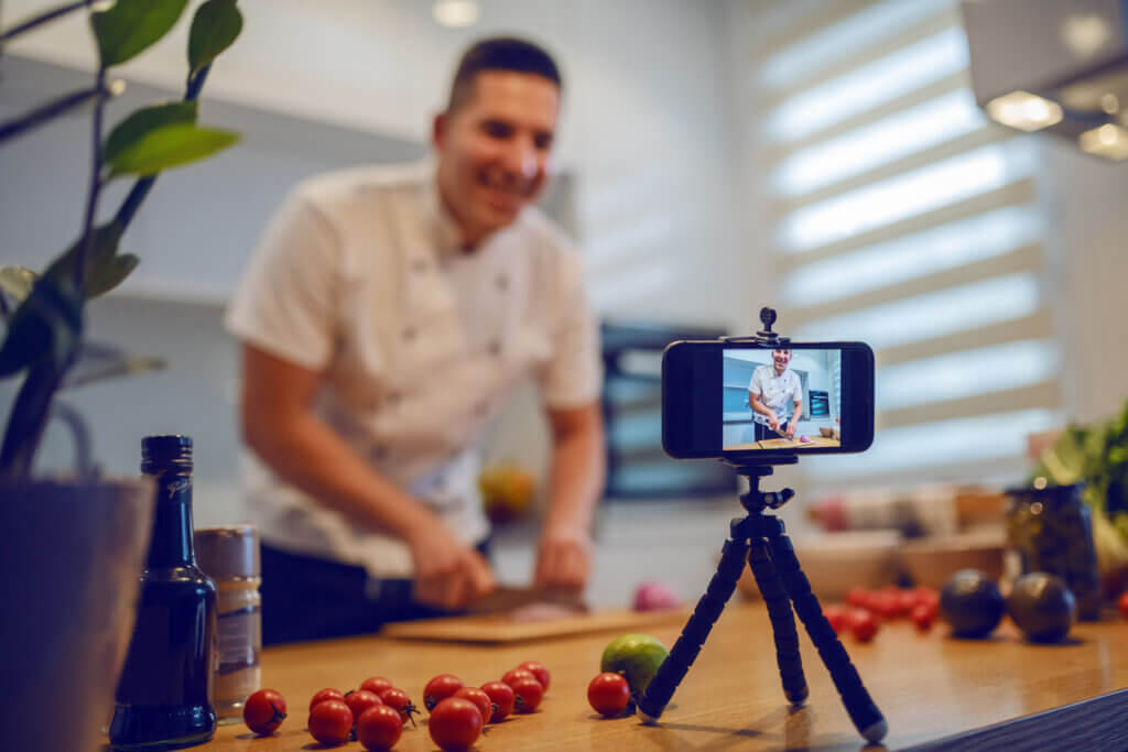 Ein Mann filmt sich per Kamera auf dem Tisch beim kochen, um es für Social Media aufzuzeichnen.