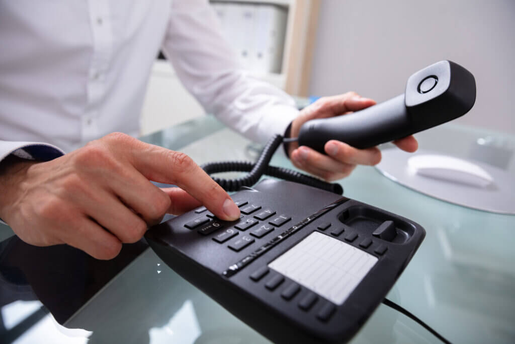 Eine Person wählt auf dem Festnetztelefon eine Nummer, den Hörer bereits in der Hand.