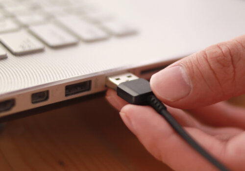 Beitragsbild 7 lustige USB-Gadgets: Nahaufnahme einer Hand, die das Datenkabel in den USB-Anschluss einsteckt