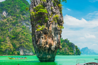 Reisender mit Selfiestick knietief im Meer in Thailand. Im Hintergrund atmenberaubende Berge. Handelt es sich um einen Travel-Vlogger?