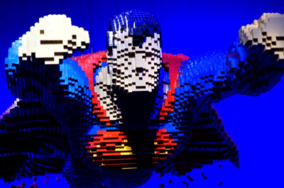 Ein aus Klemmbausteinen gebauter Superman in Flugpose vor blauem Hintergrund.