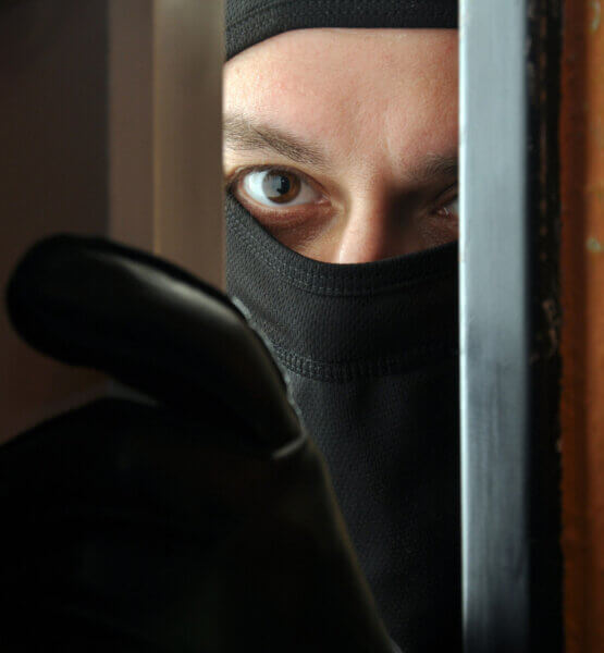 Ein maskierter Einbrecher öffnet die Tür einen Spalt weit um durchzuschauen.