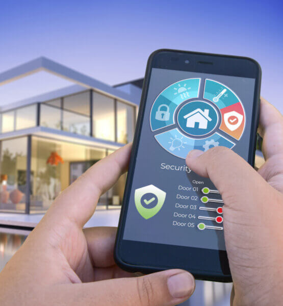 Eine Person steht mit dem Smartphone in der Hand vor einem Haus und kann damit das Smarthome, insbesondere die Sicherheit steuern.