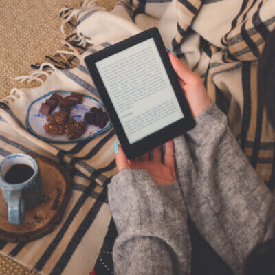 Beitragsbild die besten E-Book-Reader: Draufsicht einer Frau, die ein E-Book im E-Book-Reader mit einer Tasse Kaffee und Kakaokeksen liest. Gemütlicher Wintertag zu Hause und Hygge-Konzept. Der Text auf dem E-Book-Reader ist ein „Lorem Ipsum“