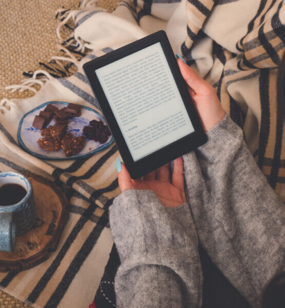 Beitragsbild die besten E-Book-Reader: Draufsicht einer Frau, die ein E-Book im E-Book-Reader mit einer Tasse Kaffee und Kakaokeksen liest. Gemütlicher Wintertag zu Hause und Hygge-Konzept. Der Text auf dem E-Book-Reader ist ein „Lorem Ipsum“