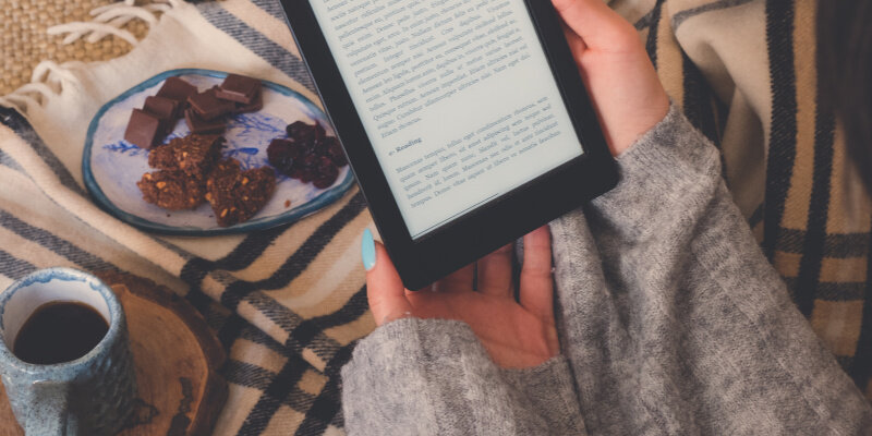 Beitragsbild die besten E-Book-Reader: Draufsicht einer Frau, die ein E-Book im E-Book-Reader mit einer Tasse Kaffee und Kakaokeksen liest. Gemütlicher Wintertag zu Hause und Hygge-Konzept. Der Text auf dem E-Book-Reader ist ein „Lorem Ipsum“