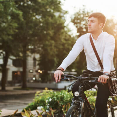 Ein Geschäftsmann fährt auf dem Rad entlang einer sehr schön begrünten Straße.