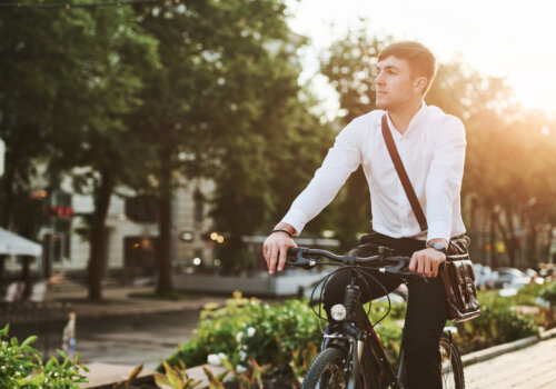 Ein Geschäftsmann fährt auf dem Rad entlang einer sehr schön begrünten Straße.