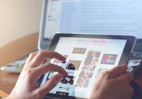 Eine Person navigiert sich mit Handgesten über eine Webapp auf einem Tablet. Im Hintergrund ist auch ein geöffneter Laptop zu sehen, auf dem ein Mailprogramm geöffnet ist.