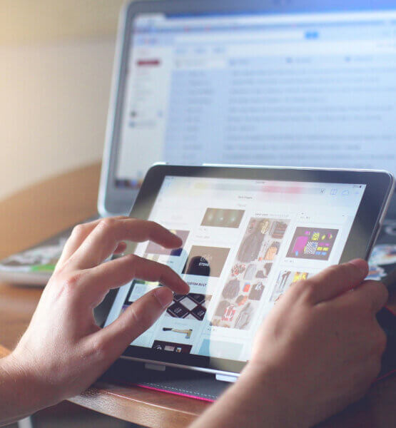 Eine Person navigiert sich mit Handgesten über eine Webapp auf einem Tablet. Im Hintergrund ist auch ein geöffneter Laptop zu sehen, auf dem ein Mailprogramm geöffnet ist.