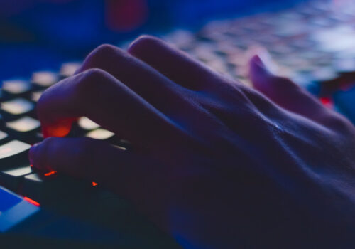 Eine Hand auf einer von innen rot beleuchteten Tastatur in einem sonst nicht beleuchtetem Raum.