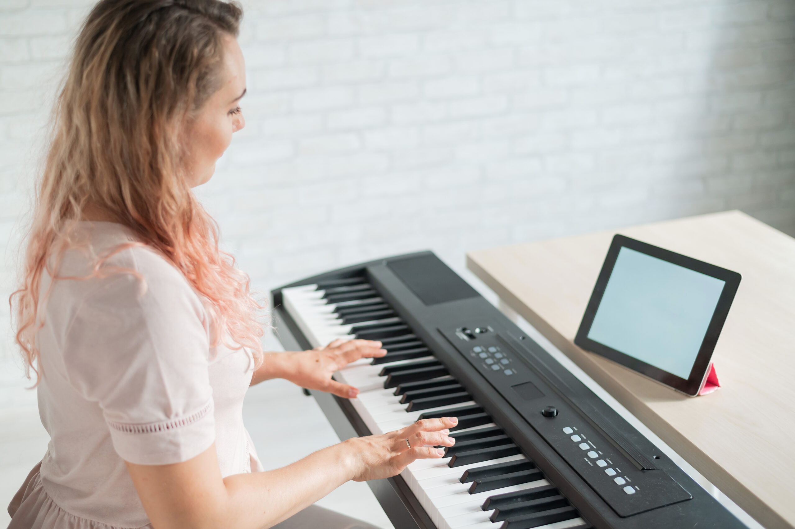 Frau sitzt an Piano und lernt auf Tablet