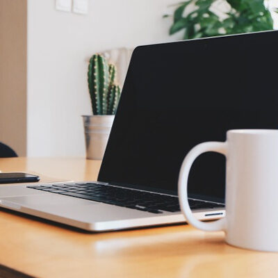 Ein Laptop zusammen mit einer Kaffeetasse und einem Smartphone auf einem Schreibtisch in einem hellen Raum.